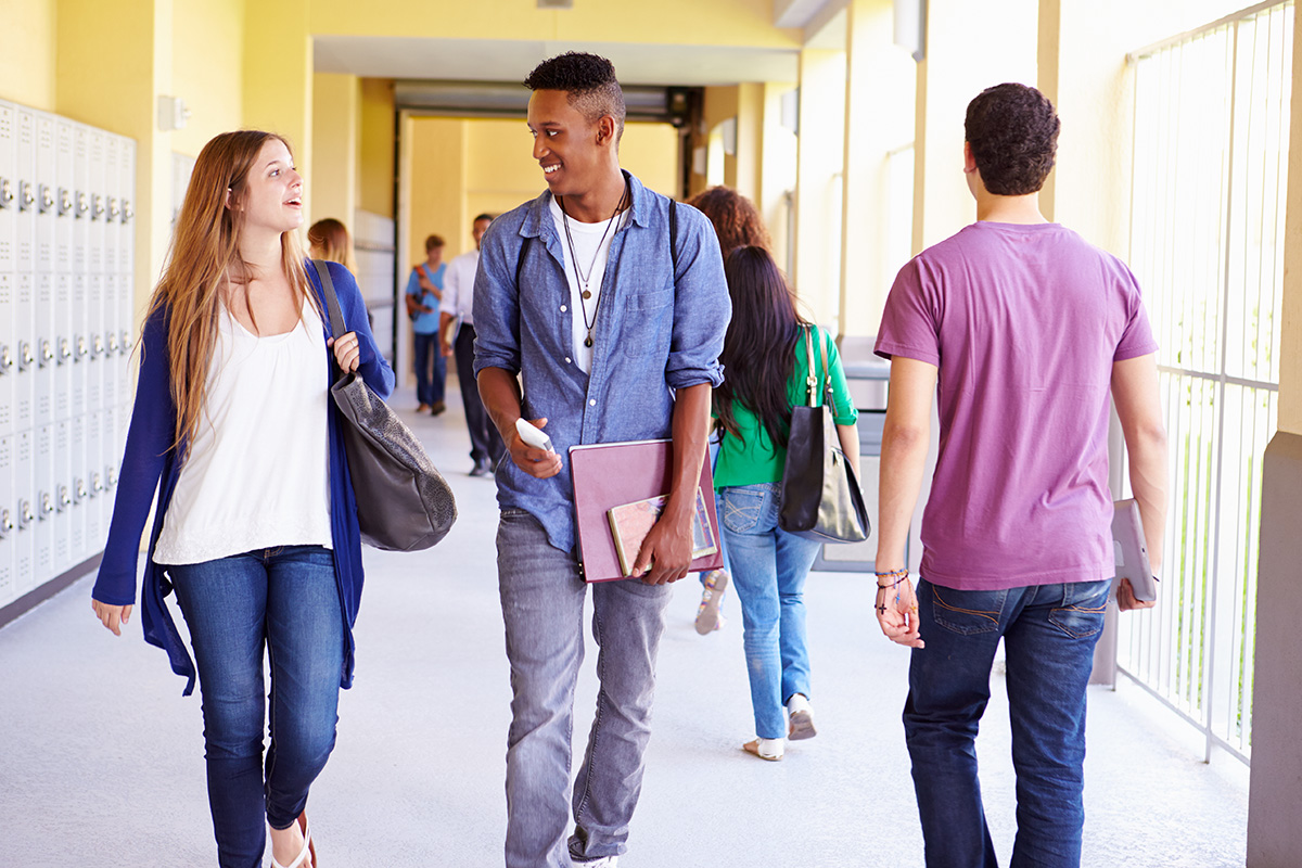 A photograph shows two students speaking to each other as they walk down a high school corridor.