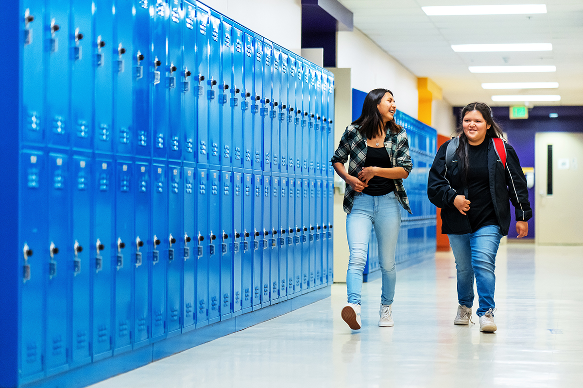 Two students walking down a hallway with blue lockers