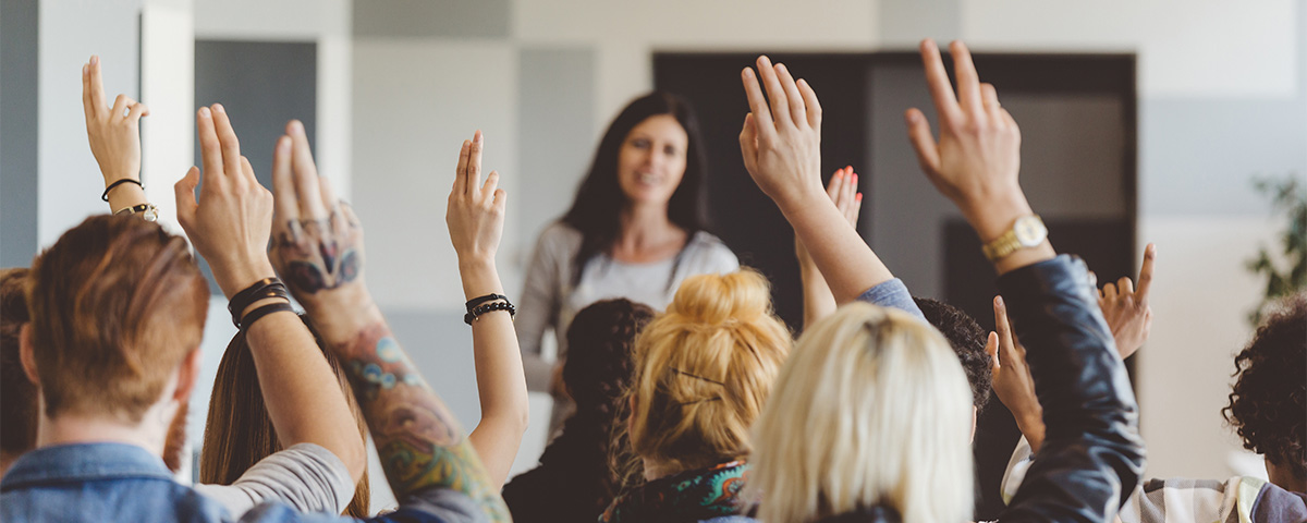 Blurred teacher standing in front of students raising their hands.