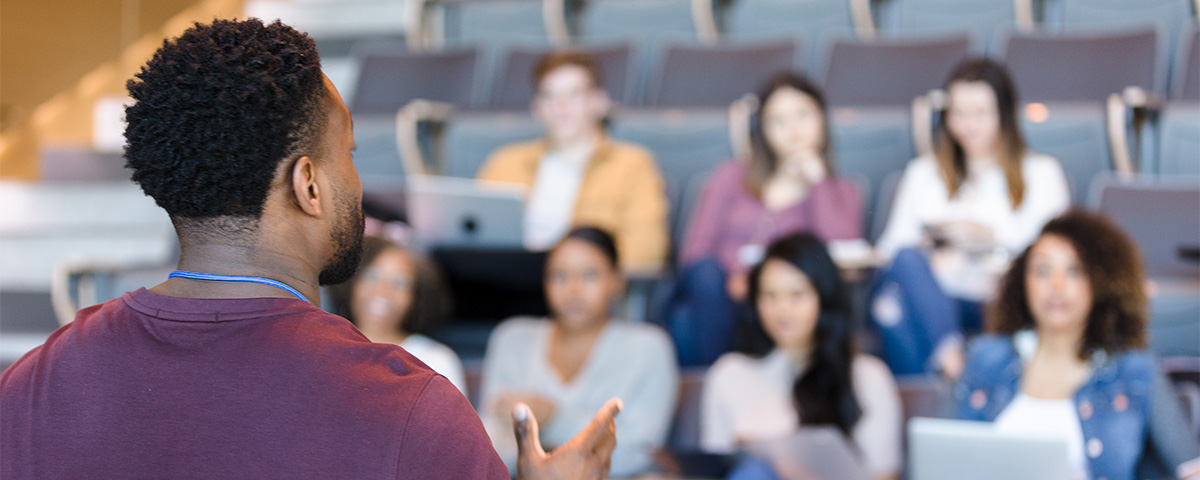 Photograph of man from behind speaking to auditorium of students.