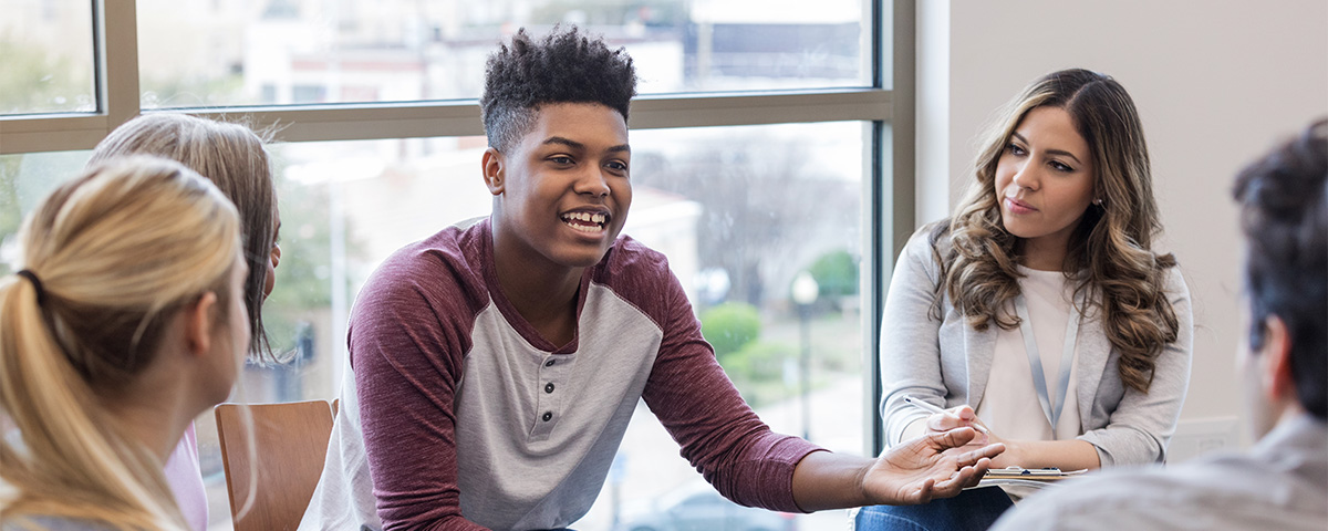 Student smiling speaking to a circle of other students.