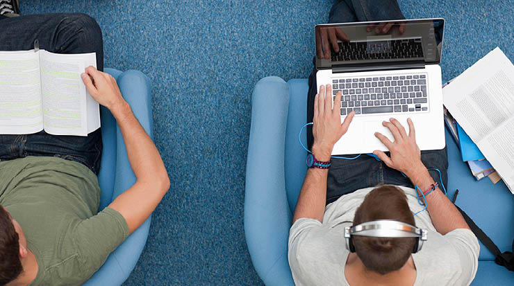 An overhead shot of two people sitting in armchairs doing homework.