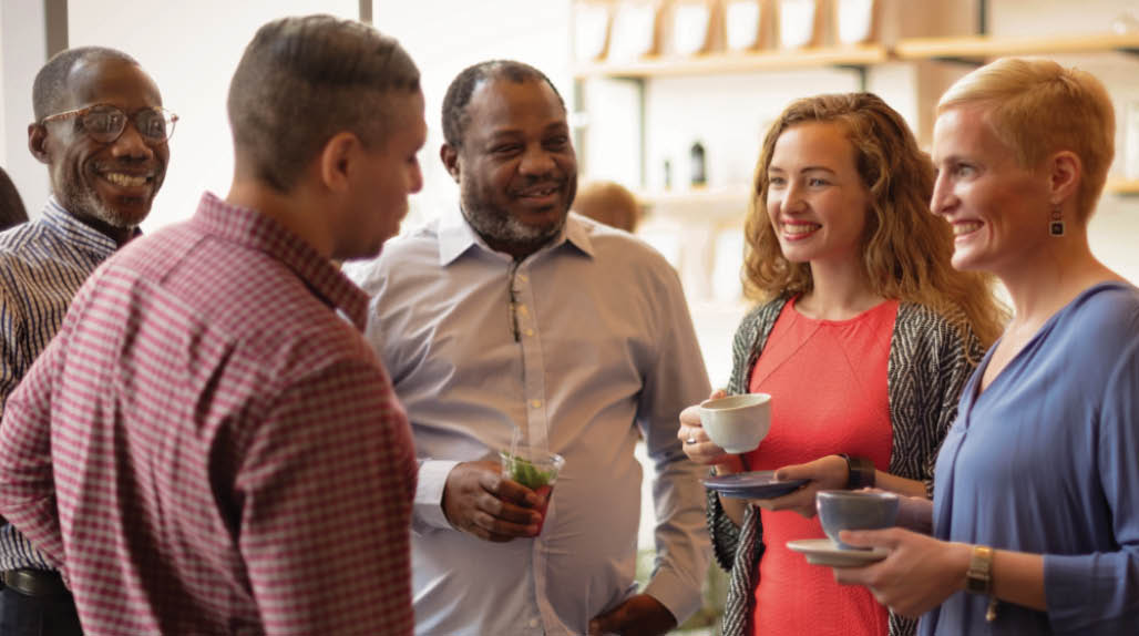 Individuals with food and coffee talking in a circle.