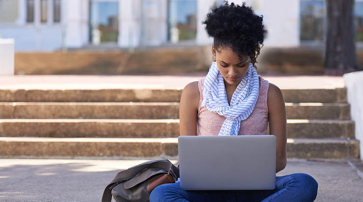 A woman sitting outside working on her laptop.