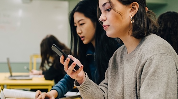 Two female students in a classroom looking at devices