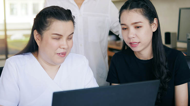 A visually impaired woman and her classmate working on a laptop.