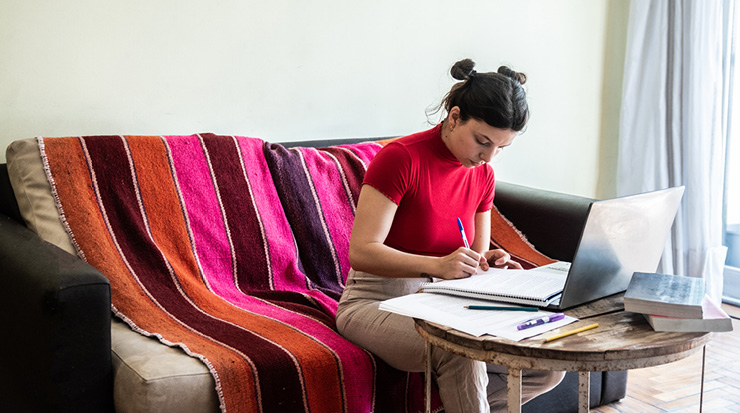 A woman is sitting on a couch working on a laptop.