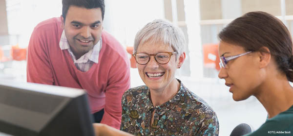 Three colleagues smiling and collaborating around a computer.