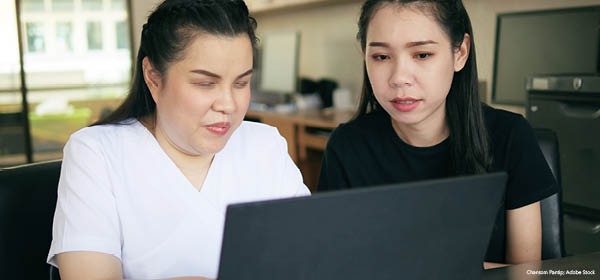 Two colleagues looking at a laptop together in an office setting.