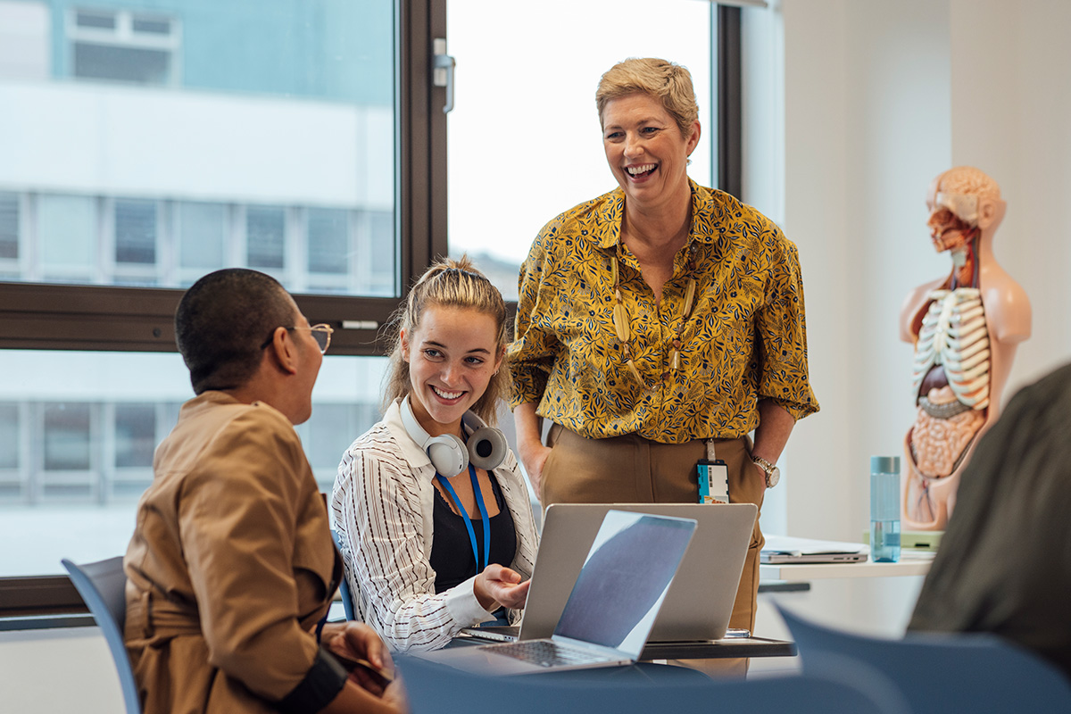 The photograph shows an instructor laughing with two students in a classroom setting