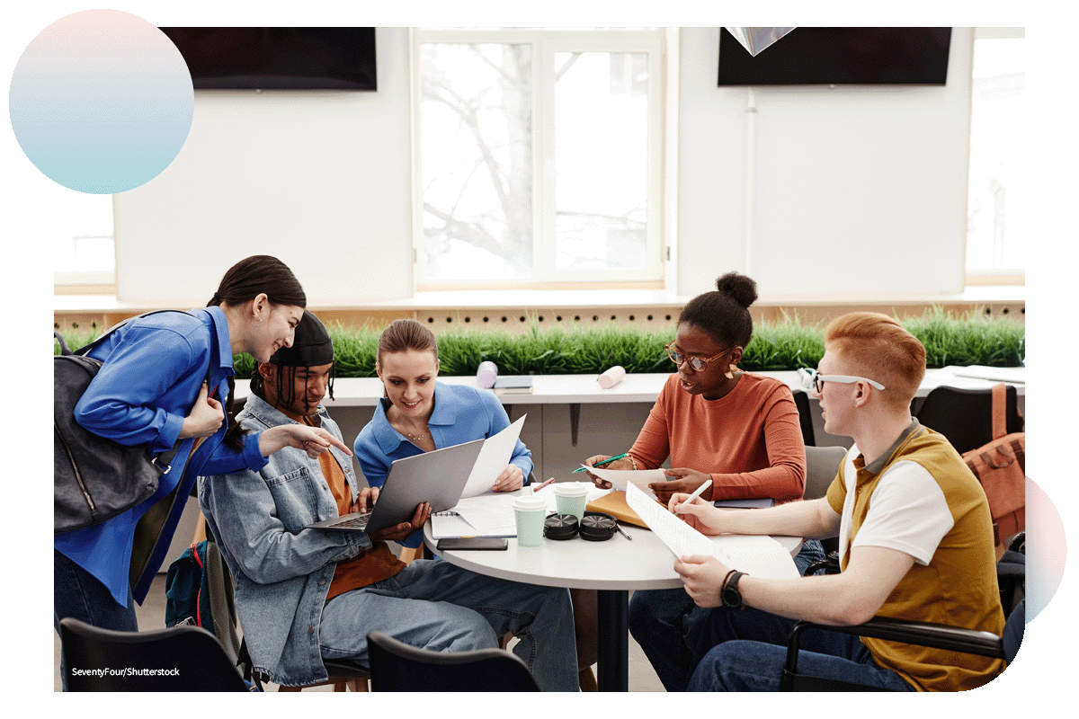 Diverse group of college students studying together at round table and discussing project