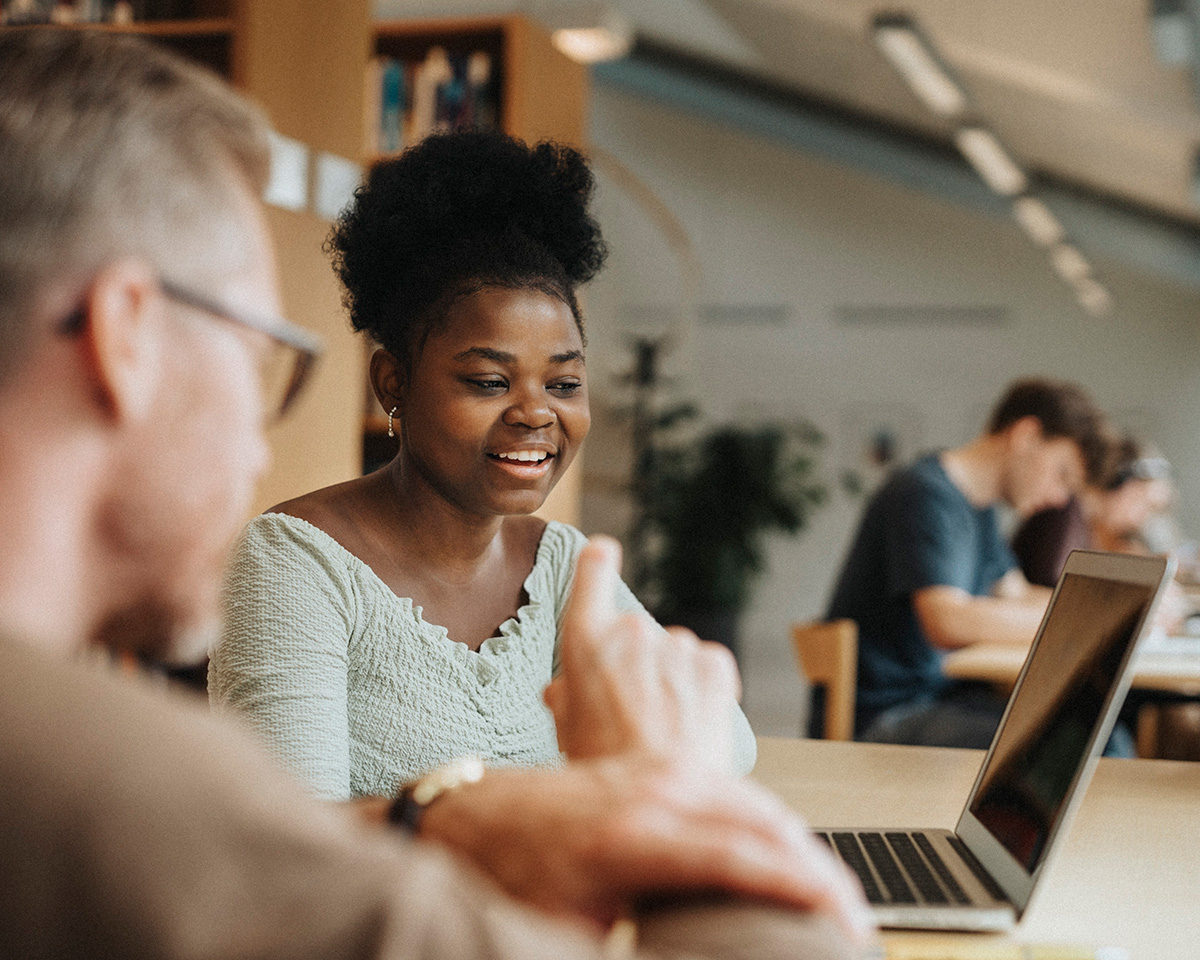 Smiling student discussing with professor over laptop in library at university