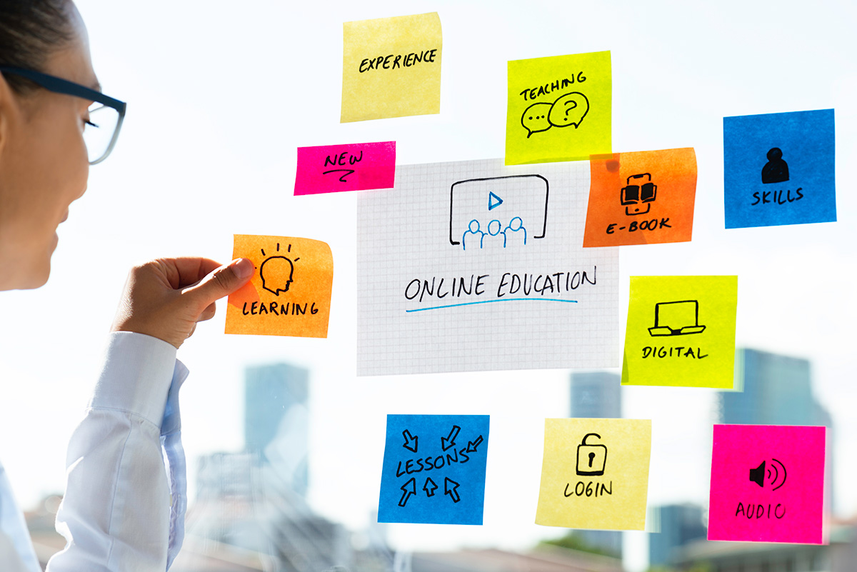 Woman is adding postits to mind map about online education on window. She is smiling and is confident. On the postits are keywords like teaching, new, experience, learning and online education written.