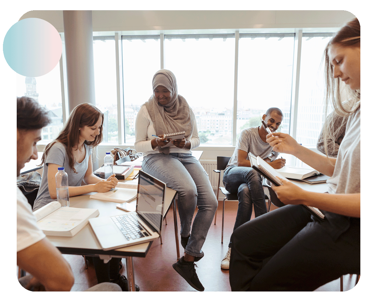 Happy young students discussing while studying at table together in university