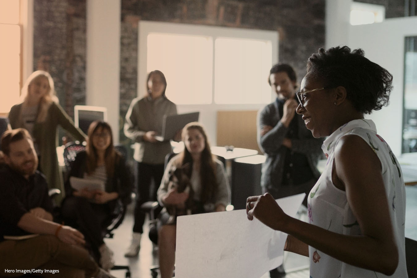 A photograph shows a classroom setup with a trainer standing in front of a group of students and explaining the information from a piece of paper.