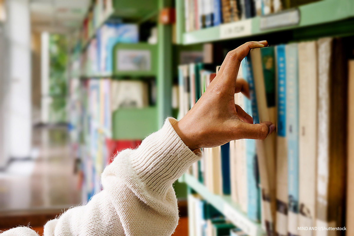 A photograph shows a person picking a book from a bookshelf in the library.