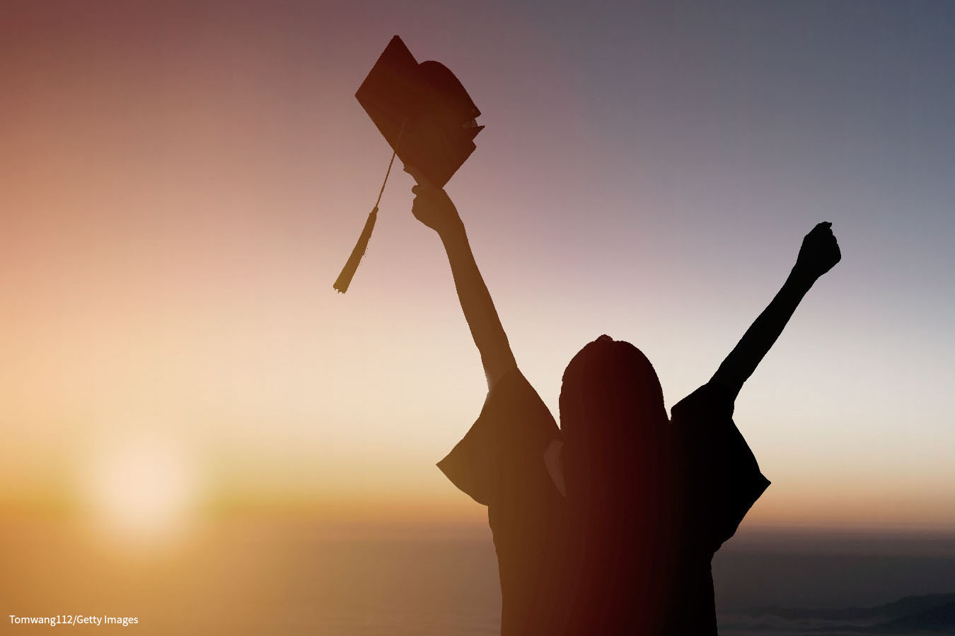 A photograph shows the rear view of a student looking towards the setting sun and celebrating graduation with a graduation cap in the right hand. 