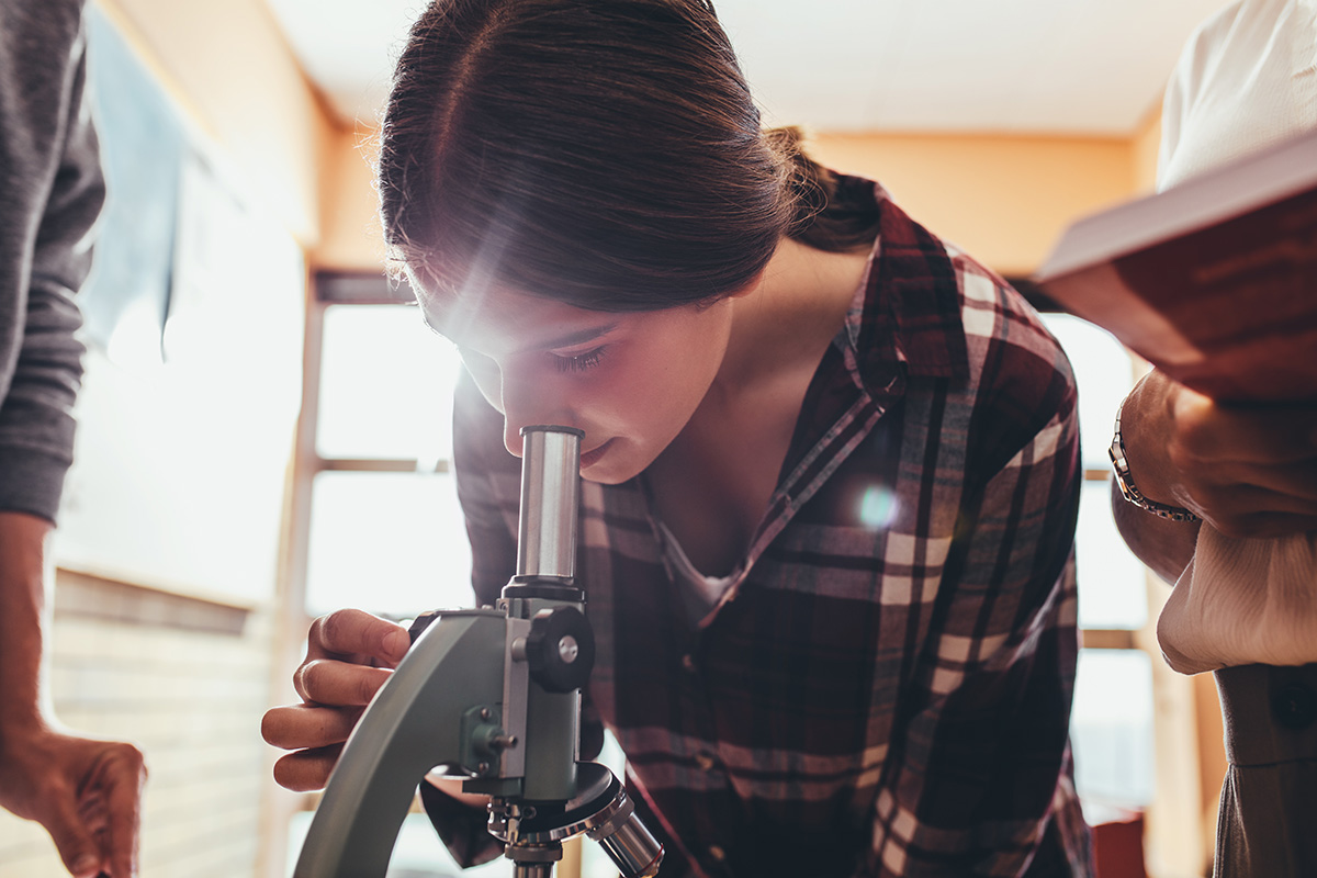 A photograph shows a girl looking through the eyepiece of a microscope.