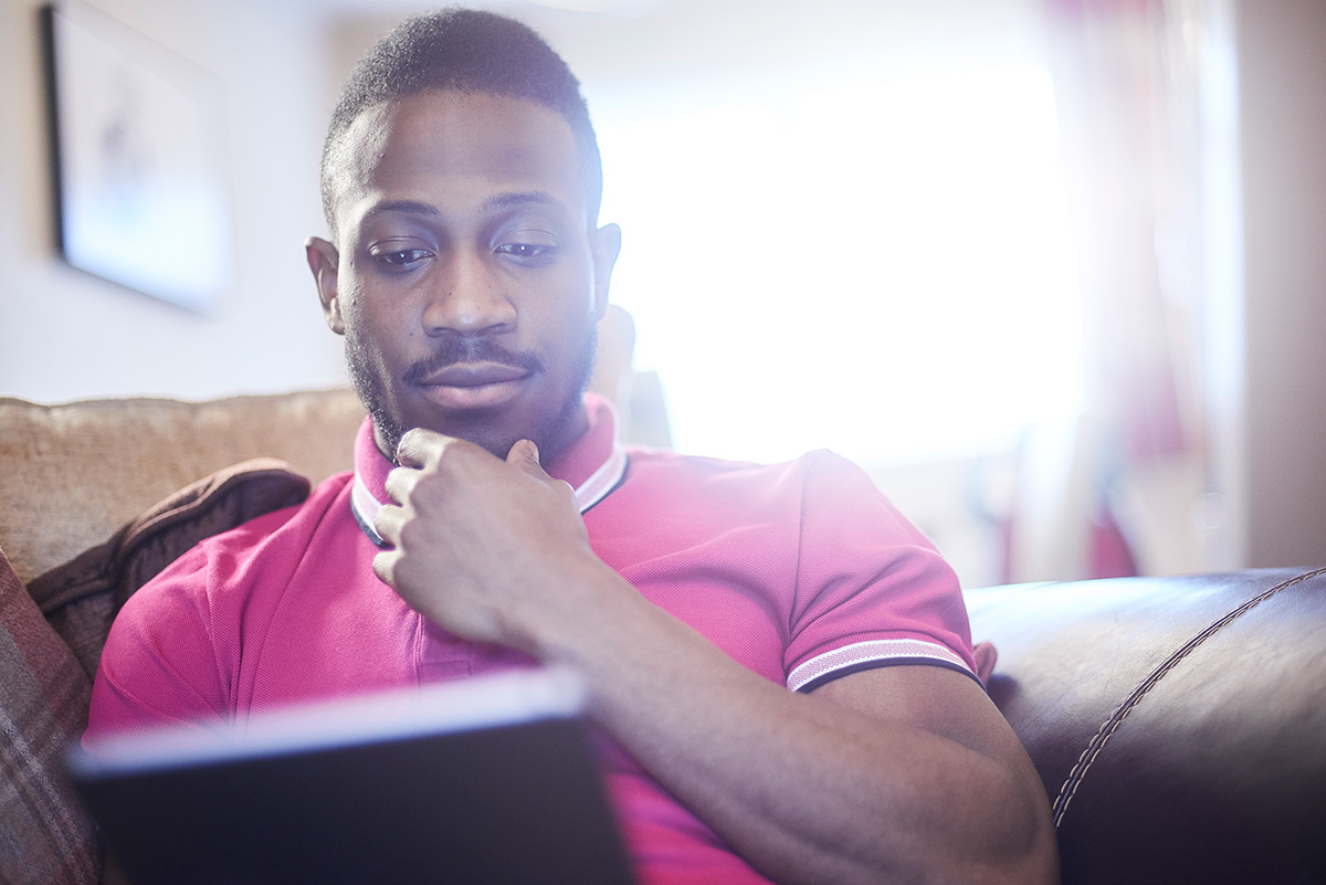 A photograph shows a man looking at the screen of a laptop and thinking something while sitting on a couch