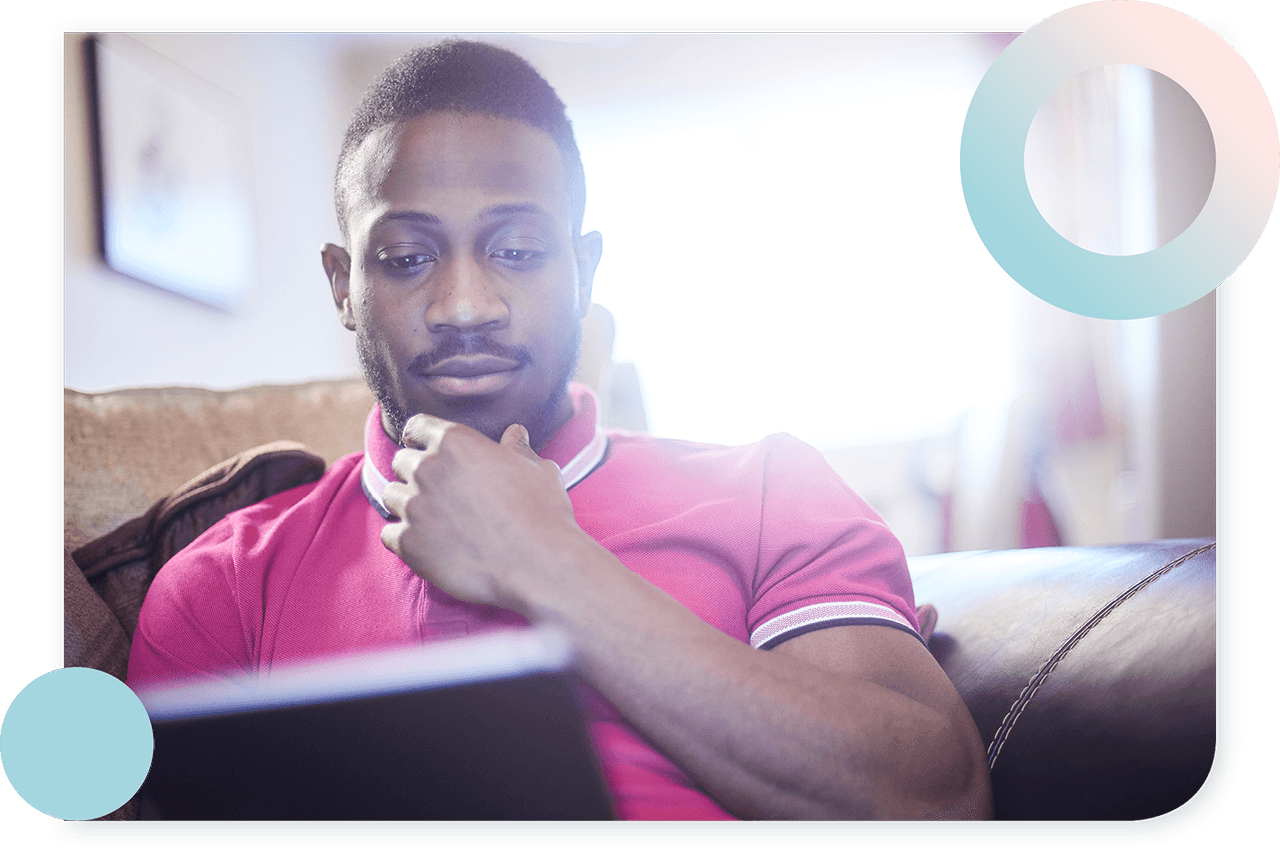 A photograph shows a man looking at the screen of a laptop and thinking something while sitting on a couch