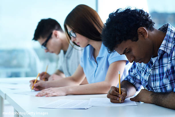 A photograph shows three students writing on a sheet while taking a test.